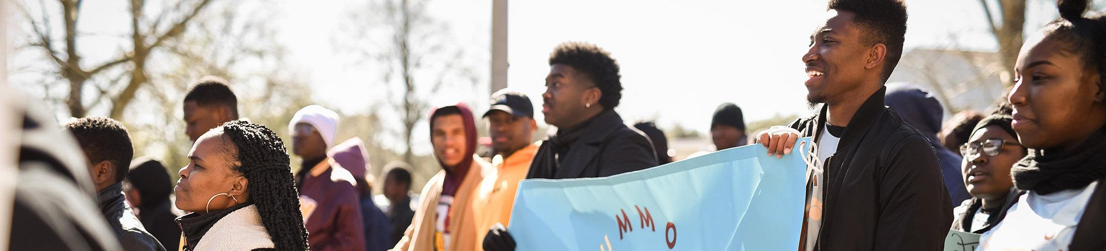 African American students marching in a parade carrying banner.